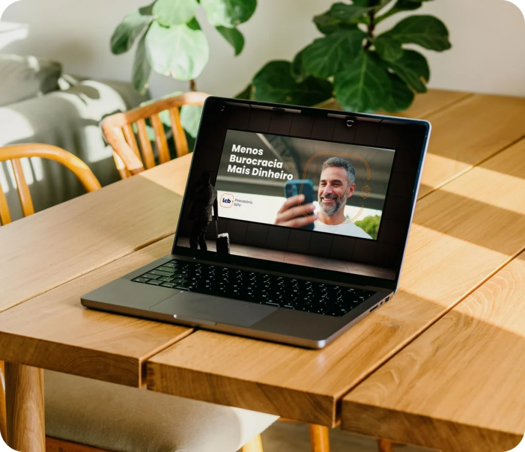 Laptop na mesa com tela exibindo homem sorridente e texto "Menos Burocracia Mais Dinheiro